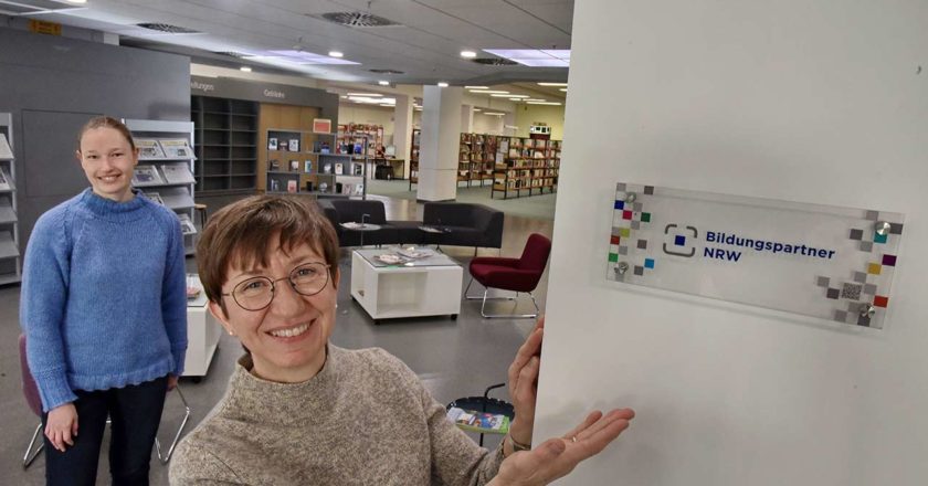 Doris Reinwald, Leiterin der Aachener Stadtbibliothek (vorne) und ihre Stellvertreterin Lisa Kmoch präsentieren die Bildungspartner-Plakette des Landes NRW.