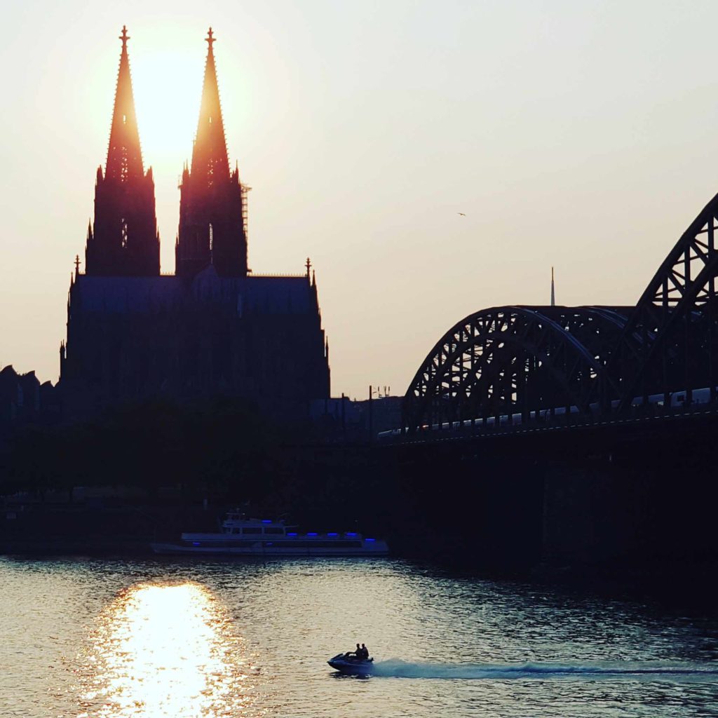 Auf dem Foto sehen Sie einen Sonnenuntergang mit Kölner Dom und Jetski auf dem Rhein