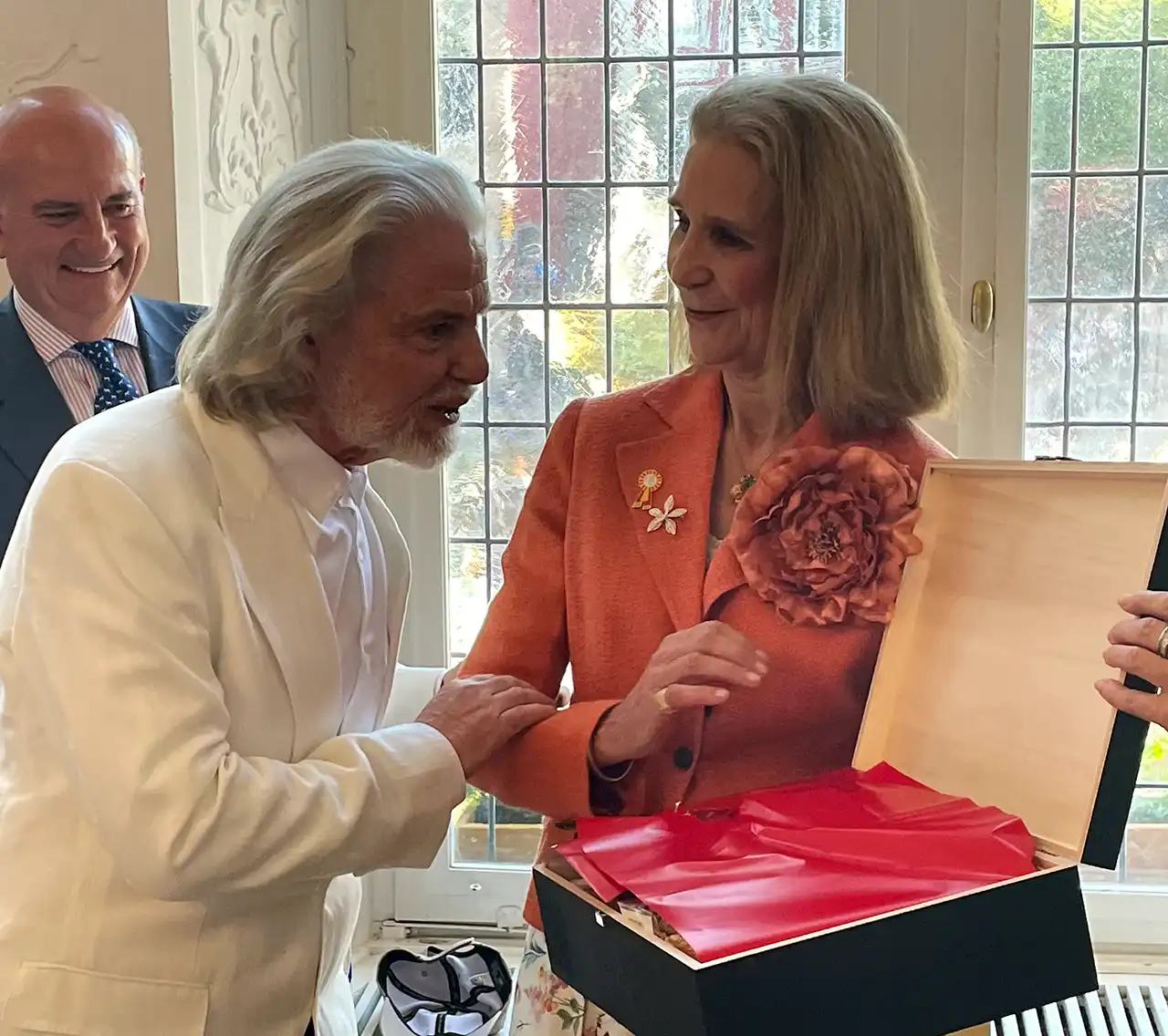 Elena von Borbón nimmt ein Geschenk von Prof. Hermann Bühlbecker entgegen – eine geöffnete, mit rotem Papier ausgelegte Truhe, beide lächeln einander an.