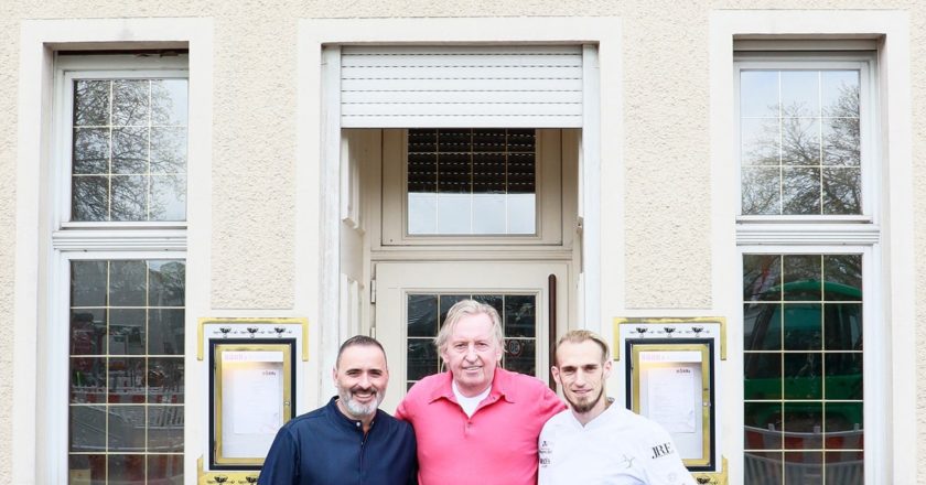 Luis Dias, Klaus Höhn und Cyril Becker stehen vor dem alten Höhns Gebäude in Köln mit dem Schild "Höhns" und "Seit 1908"