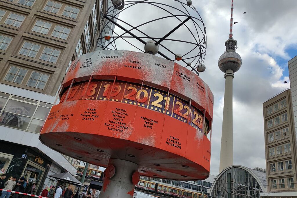 Aktivisten der 'Letzten Generation' sprühen orangerote Farbe auf die Weltzeituhr in Berlin und entrollen ein Protestbanner mit der Botschaft über den dringenden Klimawandel.