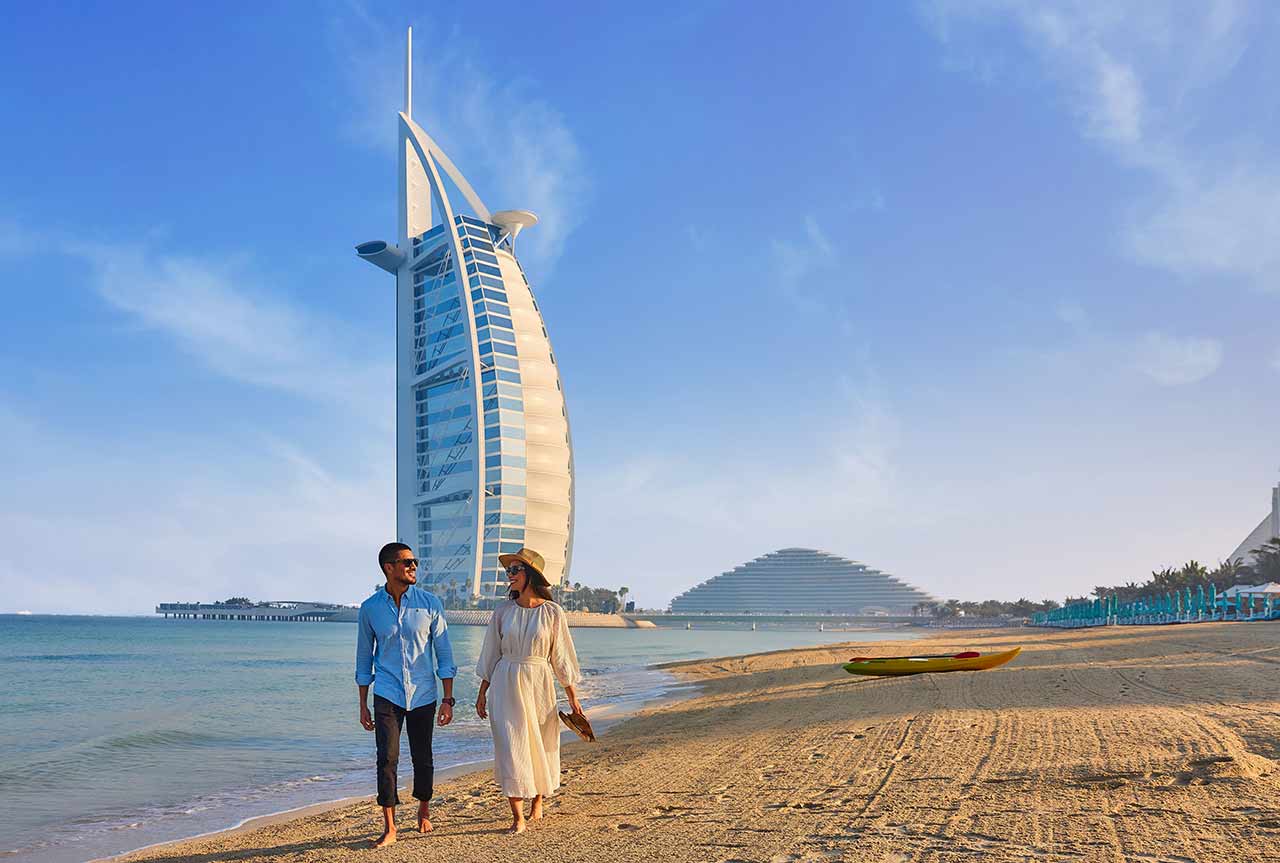 Ein Paar spaziert Hand in Hand am Strand mit Blick auf das Burj Al Arab in Dubai.