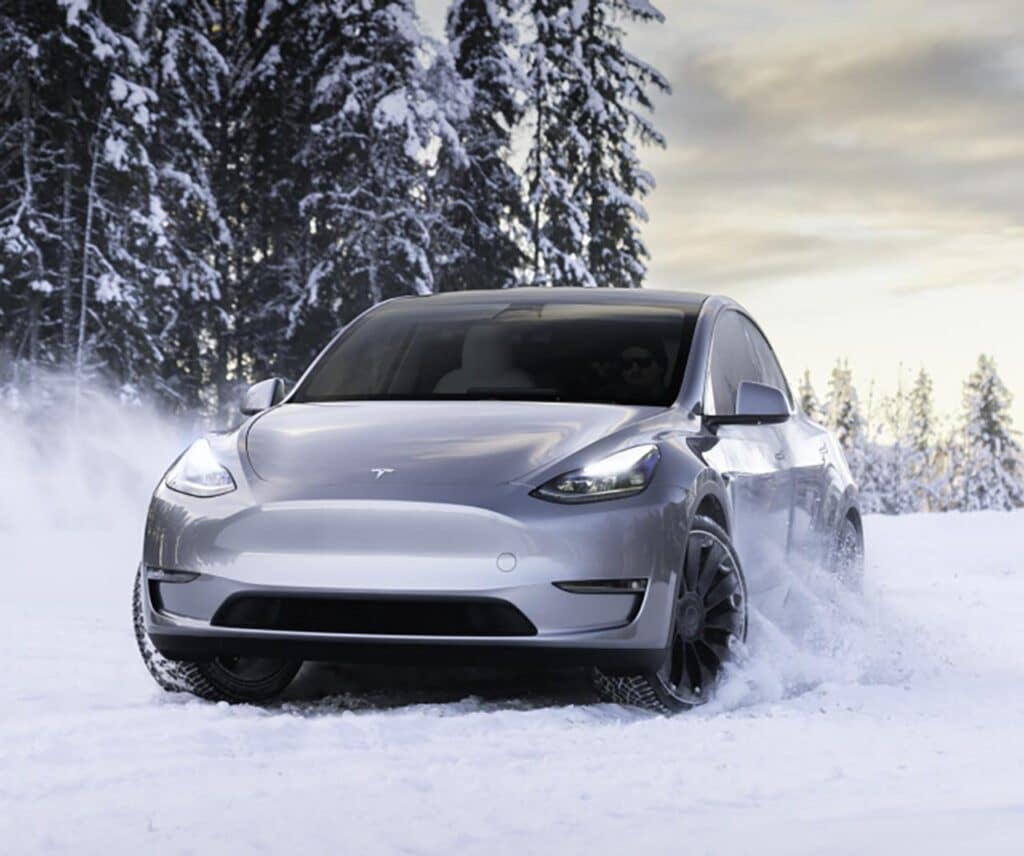 Ein silbernes Tesla Model Y fährt durch eine verschneite Waldlandschaft.