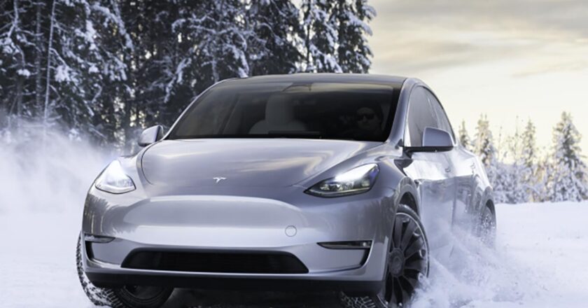 Ein silbernes Tesla Model Y fährt durch eine verschneite Waldlandschaft.