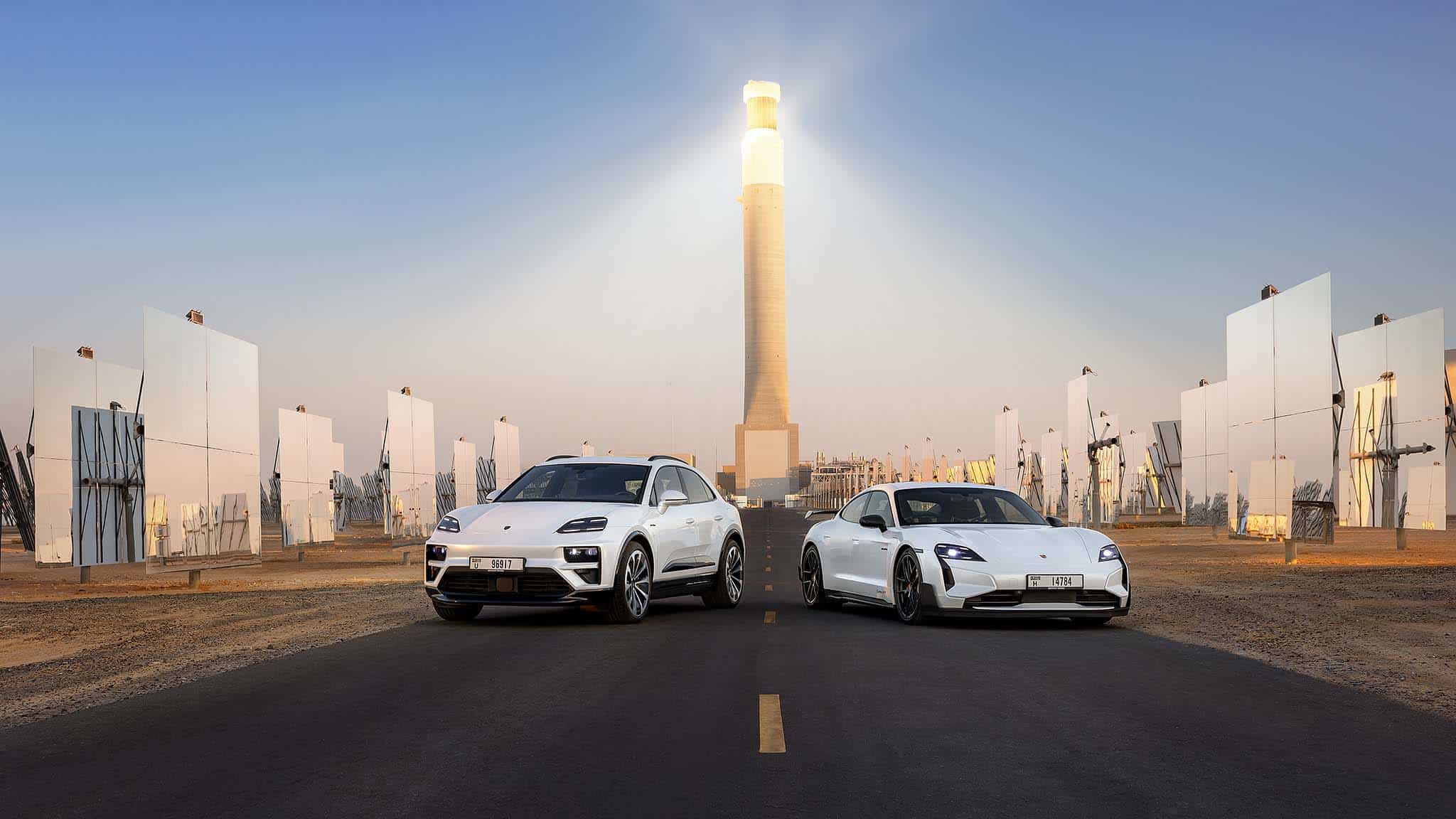 Ein weißer Porsche Macan Turbo und ein weißer Porsche Taycan Turbo GT stehen vor beeindruckenden reflektierenden Solarmodulen und einem hohen Solarturm im Mohammed-bin-Rashid-Al-Maktoum-Solarpark in Dubai. Ein weißer Porsche Macan Turbo und ein weißer Porsche Taycan Turbo GT stehen vor beeindruckenden reflektierenden Solarmodulen und einem hohen Solarturm im Mohammed-bin-Rashid-Al-Maktoum-Solarpark in Dubai.