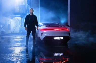 David Guetta steht neben einem weißen Porsche Taycan Turbo GT in einer stimmungsvollen, blau beleuchteten Kulisse mit reflektierendem Wasser am Boden.