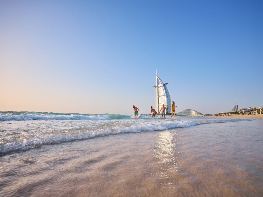 Familie genießt ihren Dubai Urlaub am Strand mit dem berühmten Hotel Burj al Arab im Hintergrund.