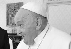 Papst Franziskus lächelt in einem Raum des Vatikans, bekleidet mit weißem Talar und Pileolus.
