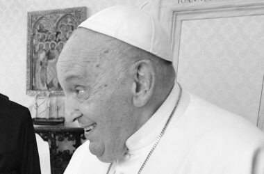 Papst Franziskus lächelt in einem Raum des Vatikans, bekleidet mit weißem Talar und Pileolus.