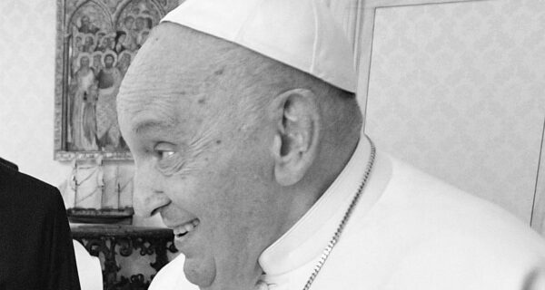 Papst Franziskus lächelt in einem Raum des Vatikans, bekleidet mit weißem Talar und Pileolus.