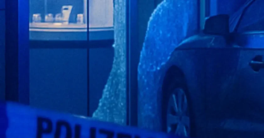 Symbolische Darstellung eines nächtlichen Einbruchs mit beschädigtem Auto vor Schaufenster und Polizeiabsperrung.