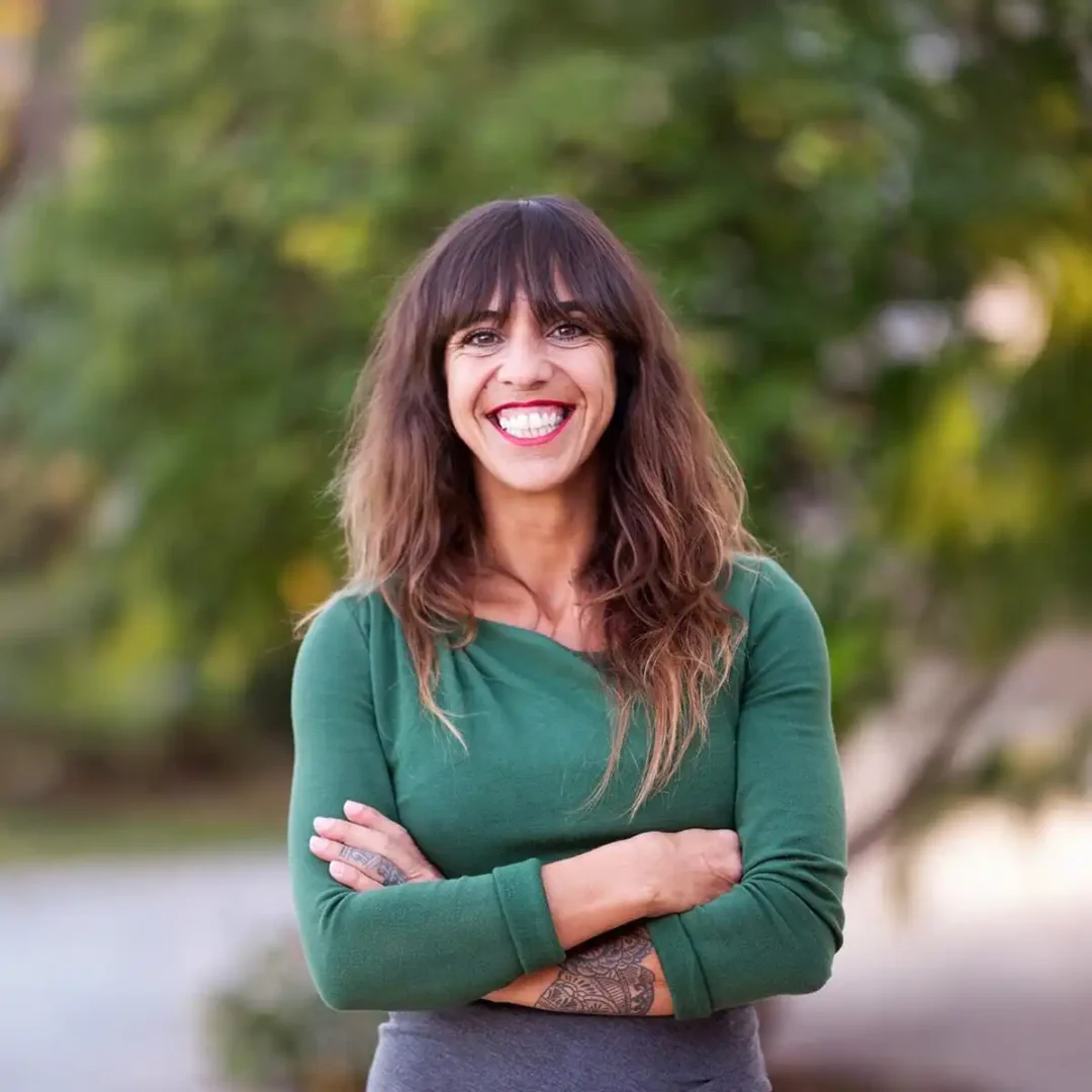 Porträt von Virginia Pérez, Innenarchitektin und Möbeldesignerin auf Mallorca, lächelnd vor grünem Hintergrund.
