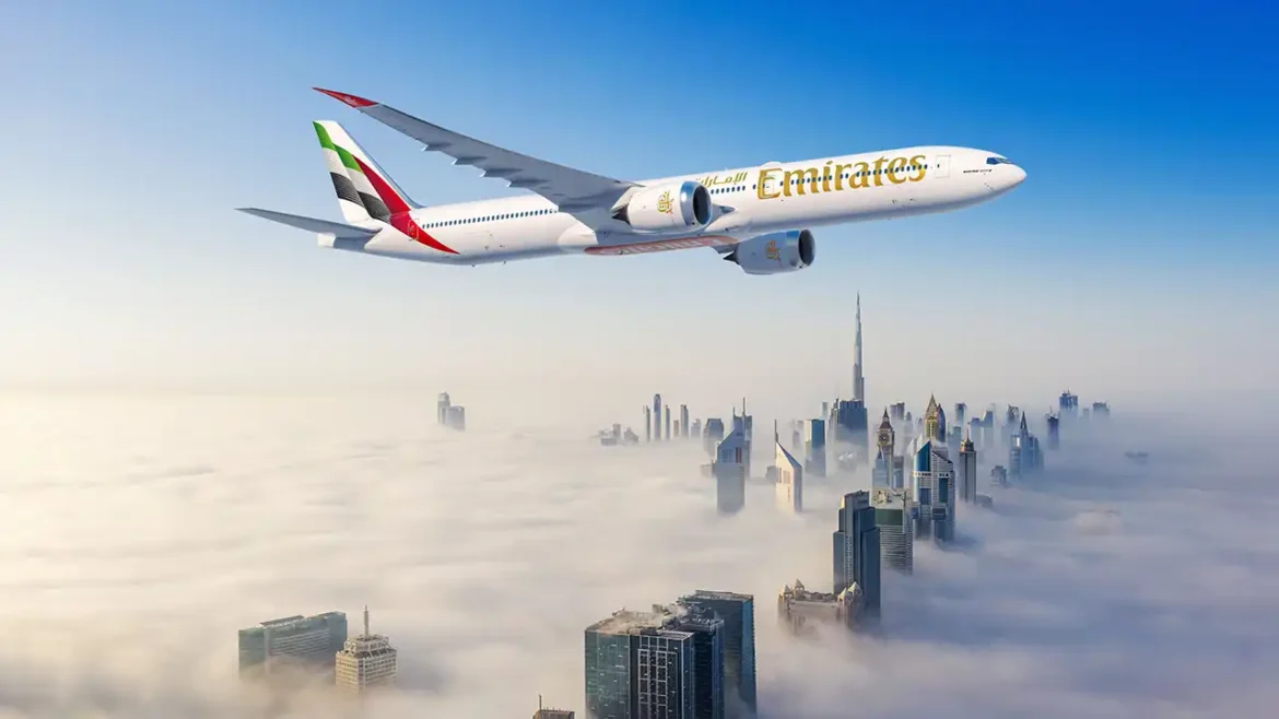 Emirates Boeing 777X im Flug über einer von Wolken bedeckten Skyline Dubais mit dem Burj Khalifa im Hintergrund.