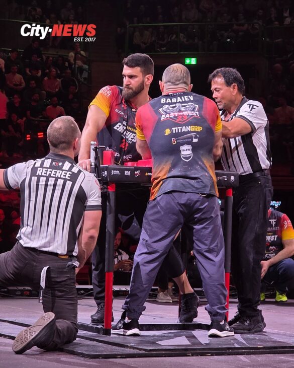 Betkili Oniani and Rustam Babaiev lock into position at the armwrestling table during East vs West 23 in Wuppertal, surrounded by referees and a focused crowd.