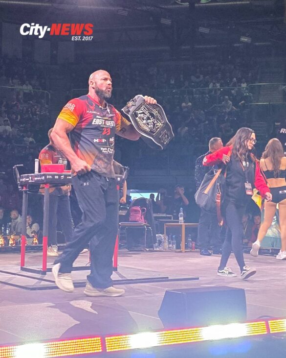 Dave Chaffee walks across the East vs West 23 stage holding the Right Arm Heavyweight World Title belt, with the arena crowd visible in the background.