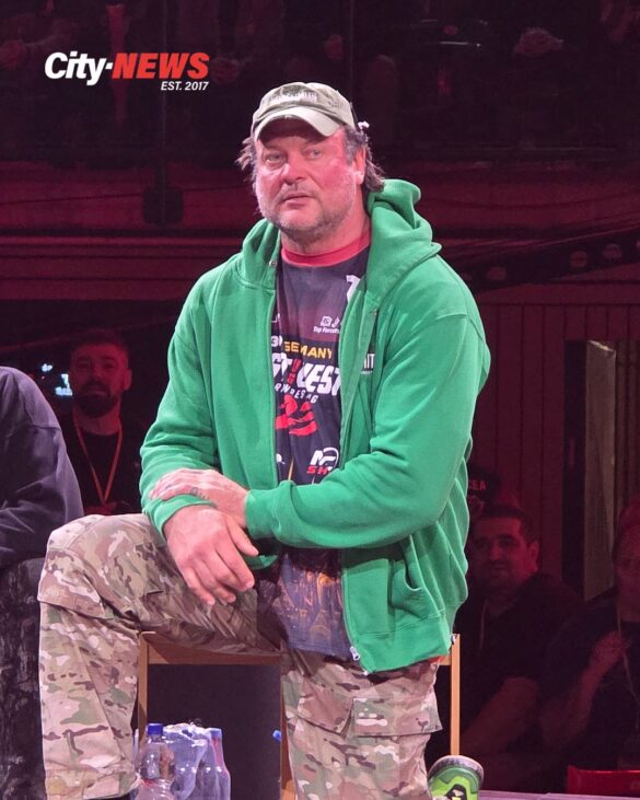 Devon Larratt stands at the East vs West 23 stage in Wuppertal wearing a green hoodie and cap, carrying the calm but charged presence of a veteran before the storm.