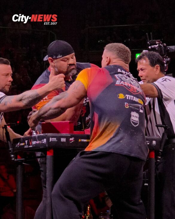 Leonidas Arkona and Brian Shaw meet at the table in a powerful close-up from East vs West 23, with referees leaning in as the moment tightens before impact.